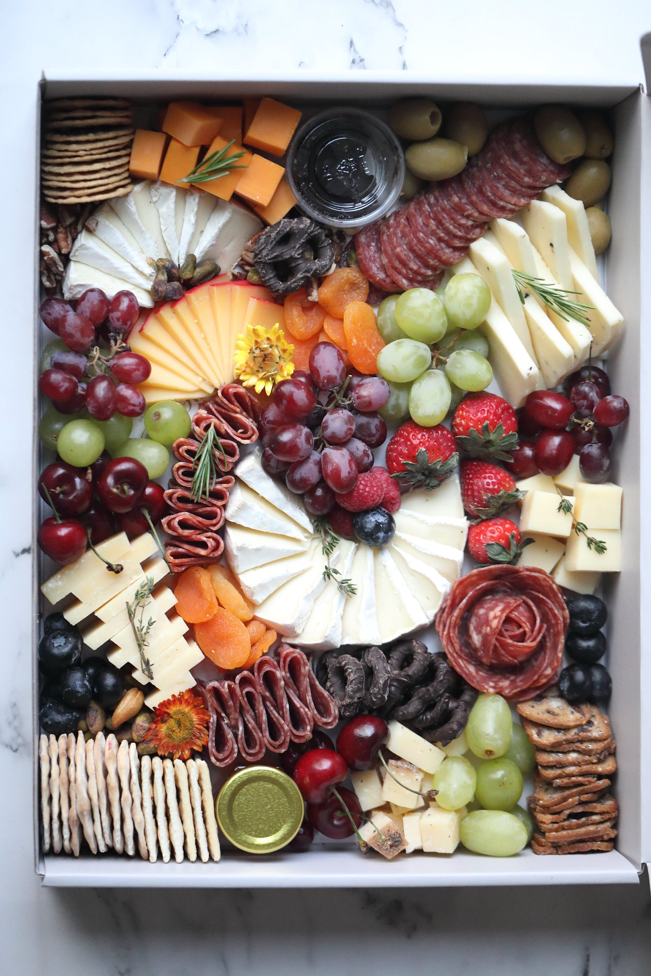 Assorted charcuterie board with meats, cheeses, fruits, and crackers in a box.